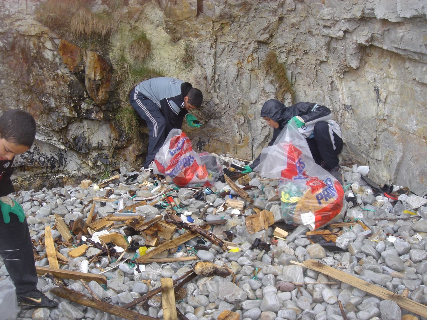 Jeunes remplissant des sacs de déchets au pied d'une falaise, sur les galets