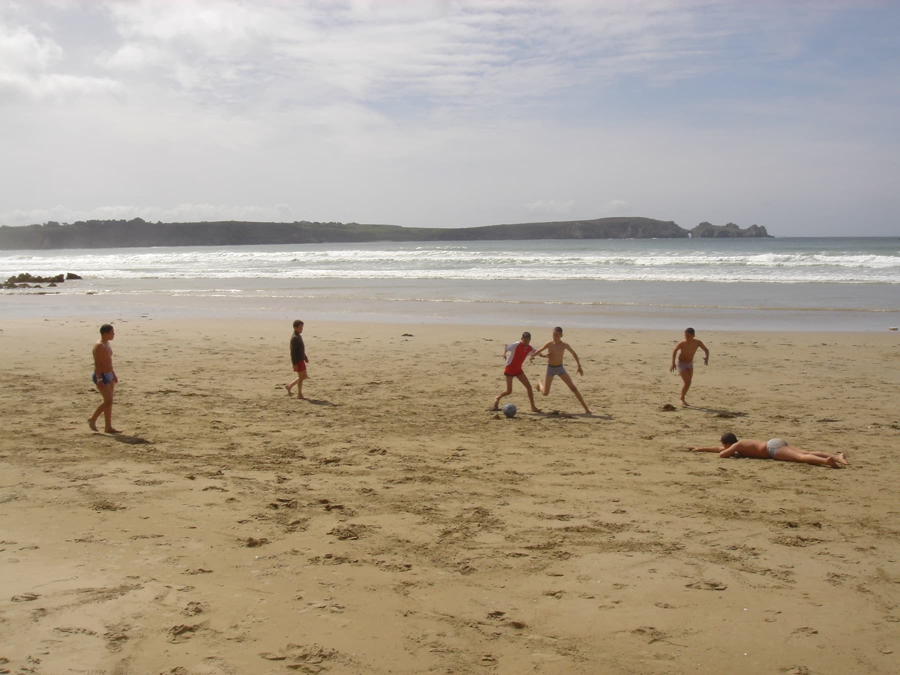 Partie de football sur le sable, pointe rocheuse au fond