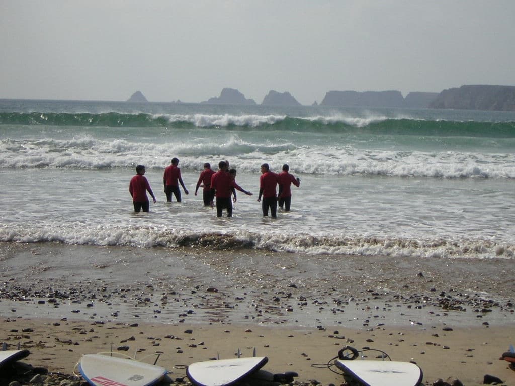 Groupe en combinaison entrant dans les vagues, planches de surf posées sur le sable
