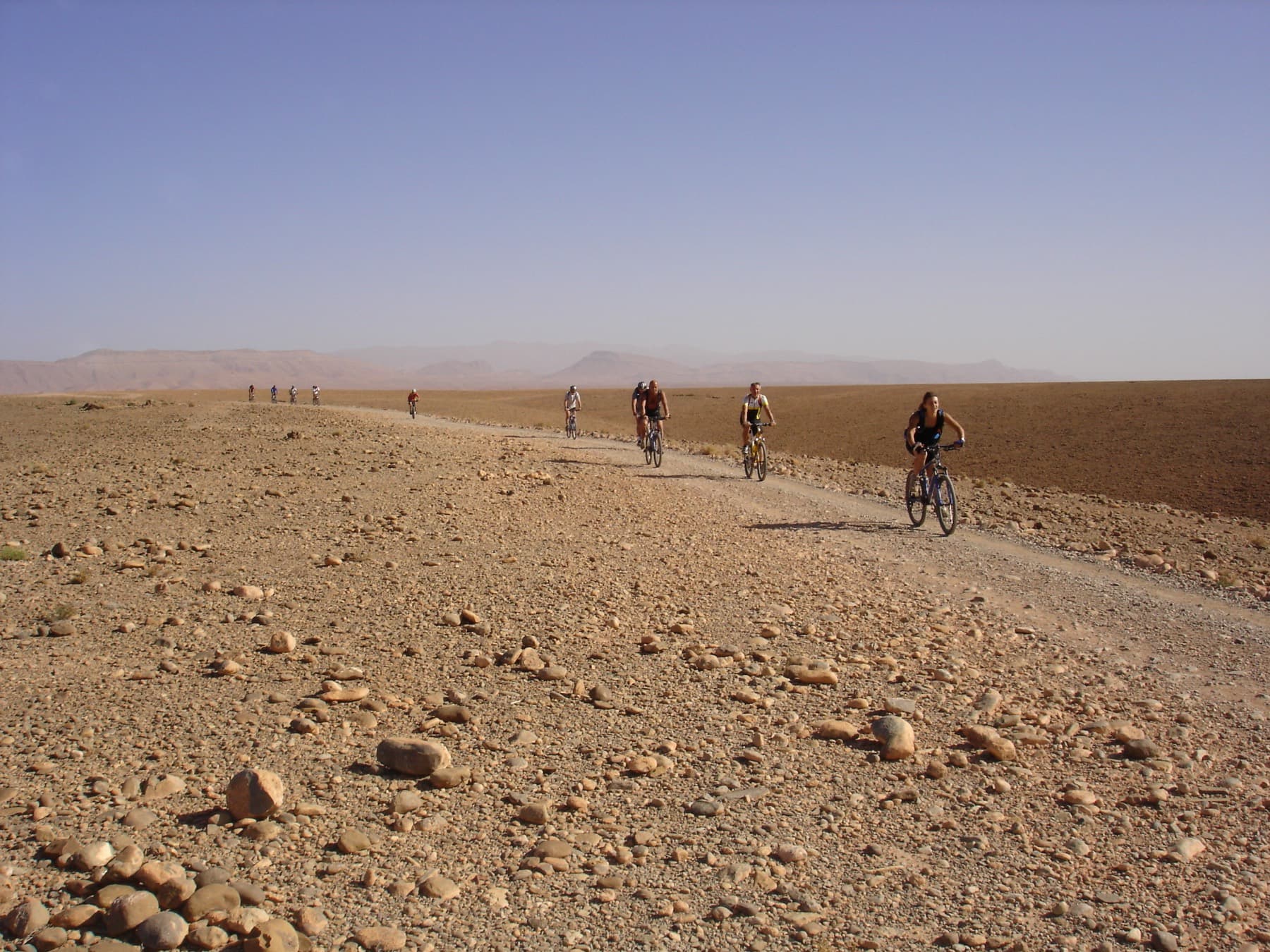 Groupe à vélo sur une piste caillouteuse, montagnes à l'horizon
